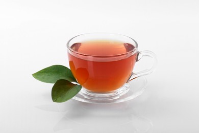 Tasty tea in cup and green leaves on white background