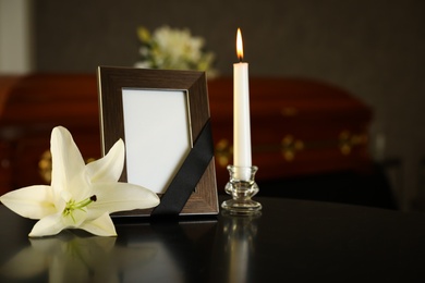 Black photo frame with burning candle and white lily on table in funeral home