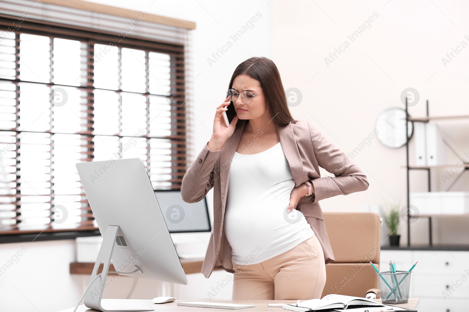 Photo of Young pregnant woman suffering from pain while working in office