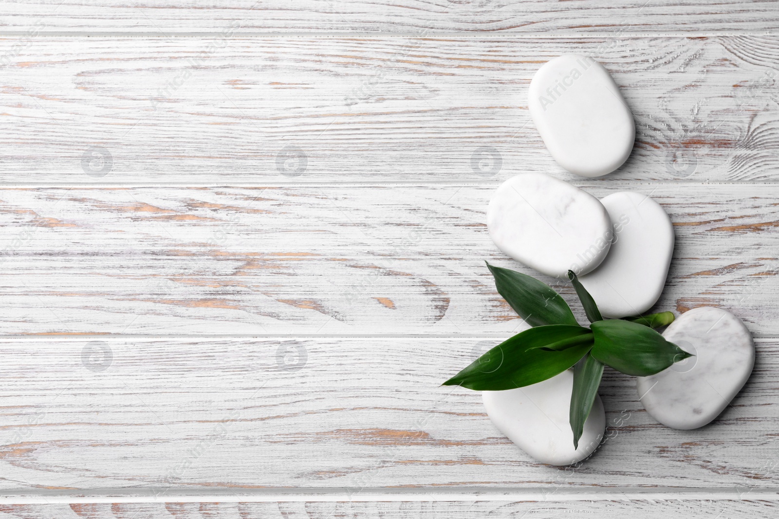 Photo of Spa stones and bamboo leaves on white wooden table, flat lay. Space for text