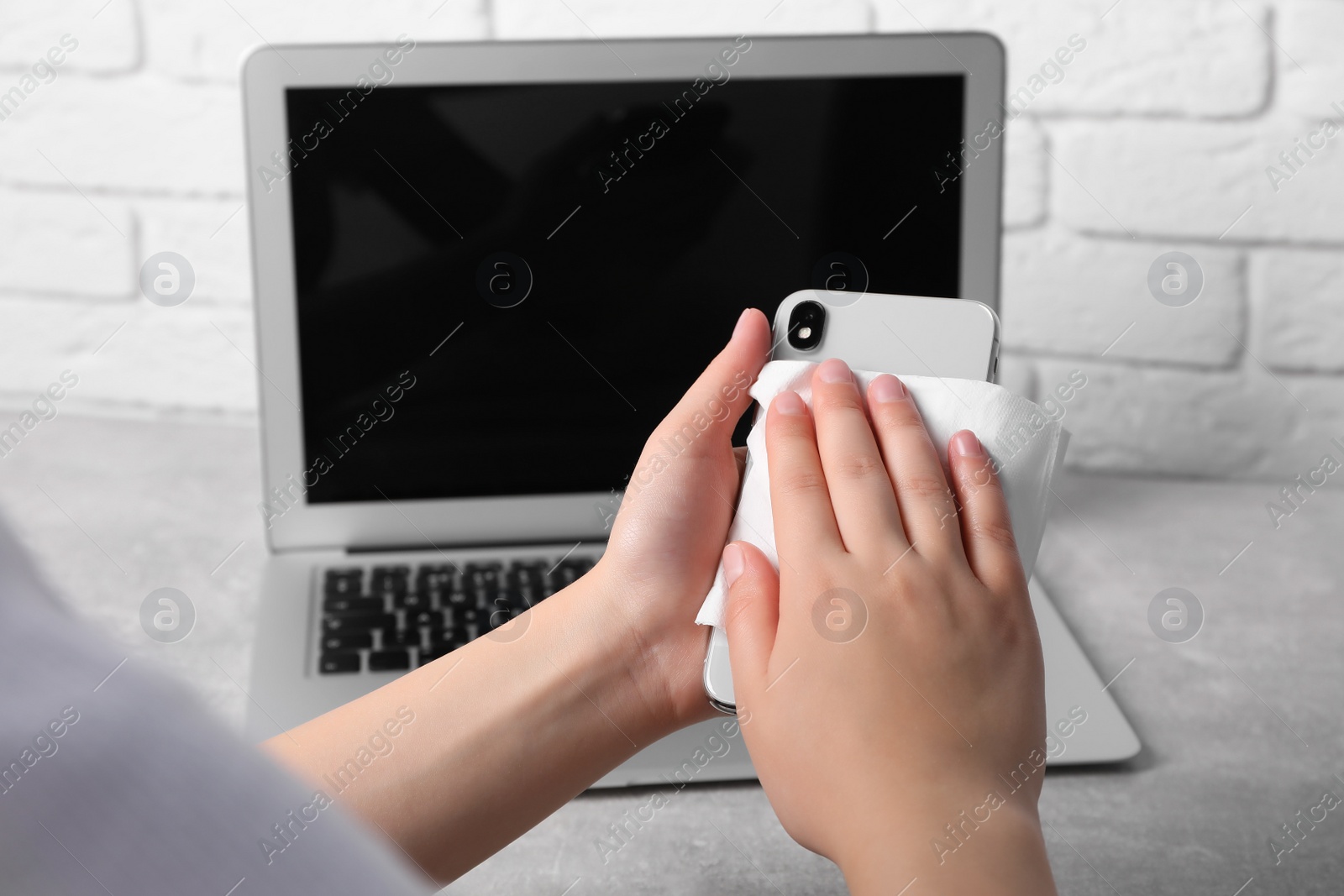 Photo of Woman wiping smartphone with paper near white brick wall, closeup