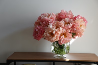 Photo of Beautiful pink peonies in vase on table near white wall, space for text