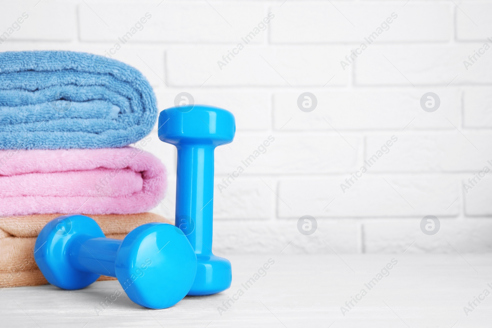 Photo of Stylish dumbbells and towels on table against brick wall, space for text. Home fitness