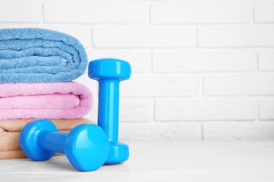 Stylish dumbbells and towels on table against brick wall, space for text. Home fitness