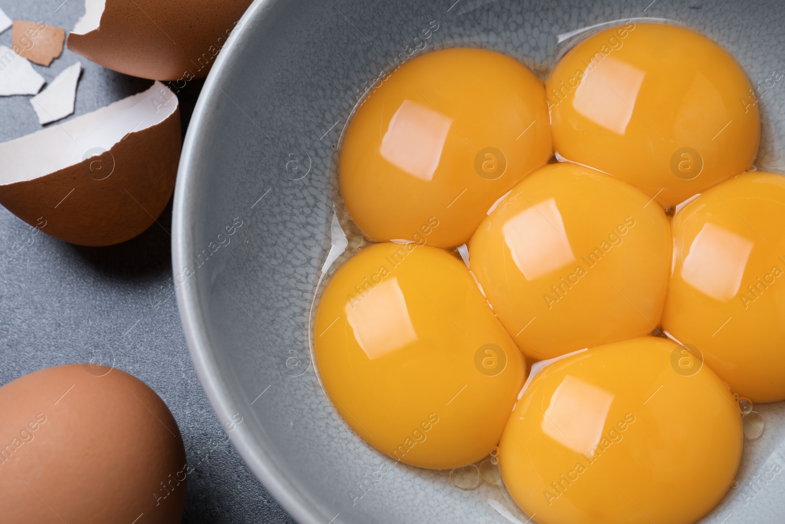 Photo of Bowl with raw egg yolks on grey table, closeup
