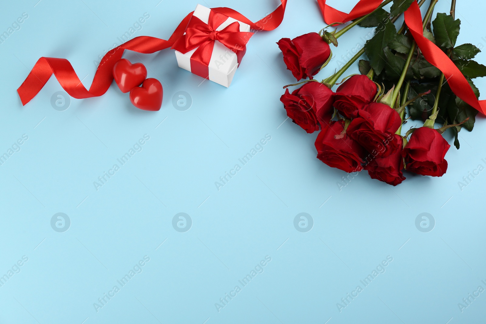 Photo of Flat lay composition with beautiful red roses and gift box on light blue background, space for text. Valentine's Day celebration