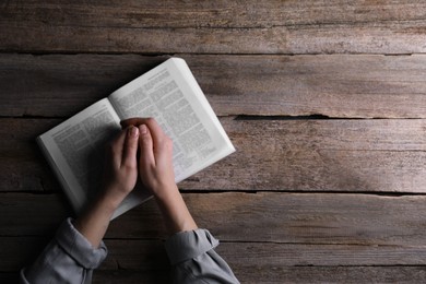 Religion. Christian woman praying over Bible at wooden table, top view. Space for text