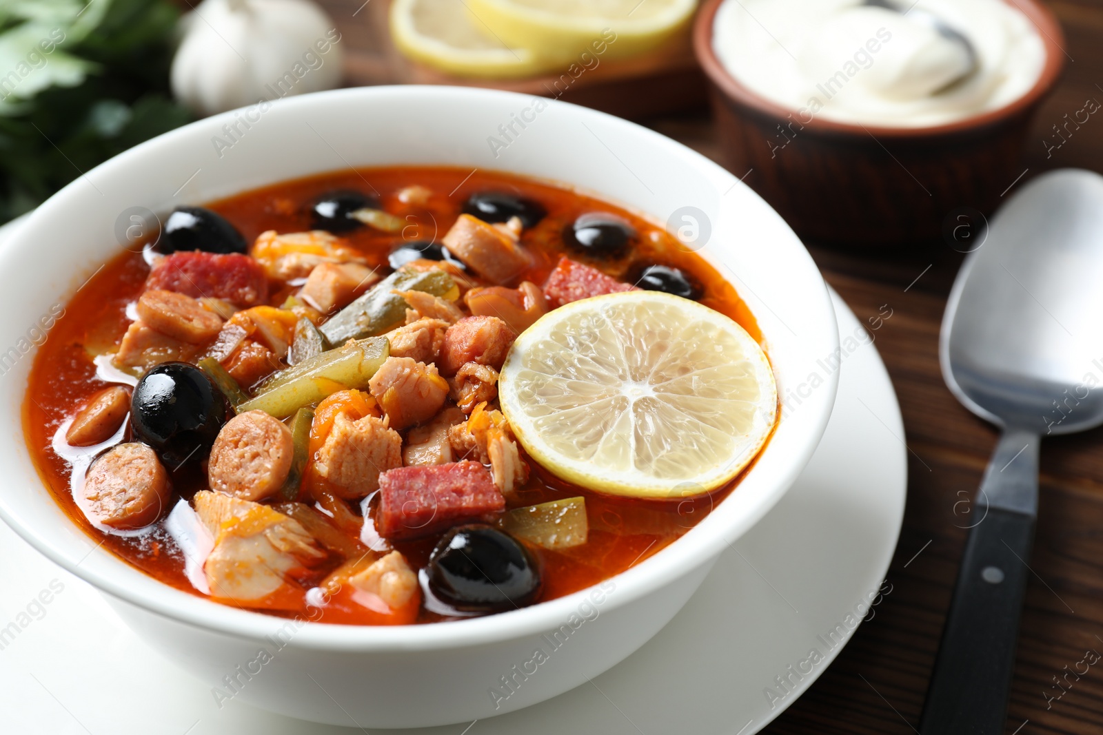 Photo of Meat solyanka soup with sausages, olives and vegetables served on table, closeup