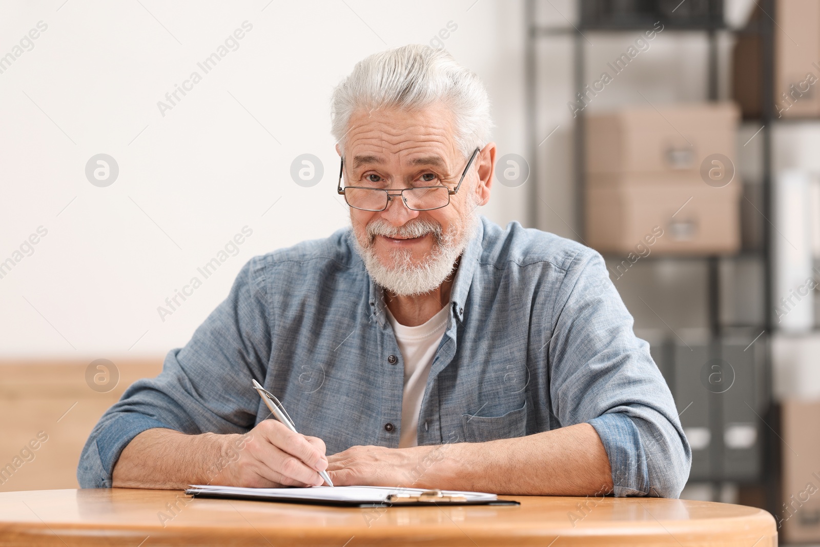 Photo of Senior man signing Last Will and Testament at table indoors