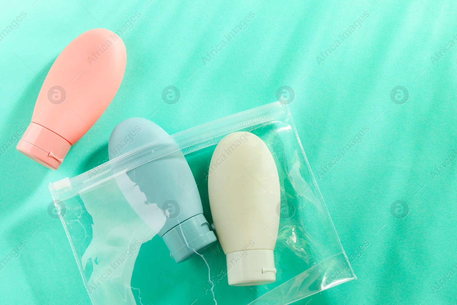 Photo of Cosmetic travel kit with plastic bag on turquoise background, top view. Space for text