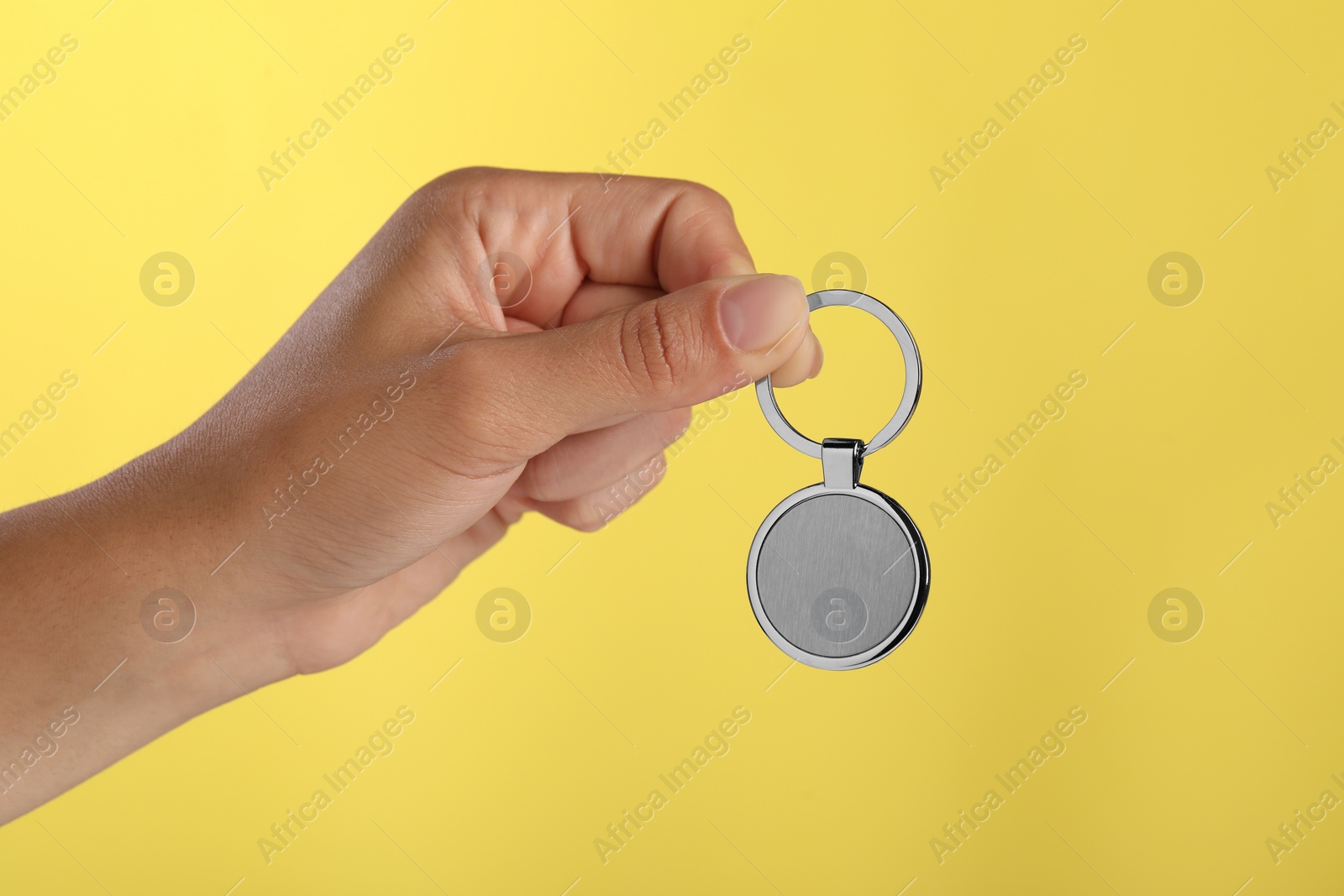 Photo of Woman holding metallic keychain on yellow background, closeup