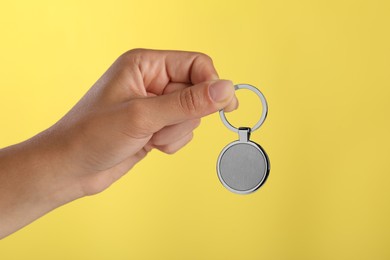 Photo of Woman holding metallic keychain on yellow background, closeup