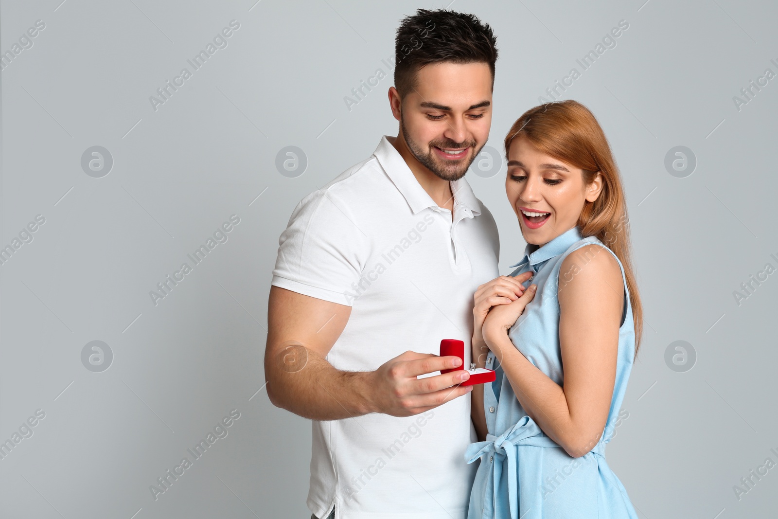 Photo of Man with engagement ring making marriage proposal to girlfriend on light grey background