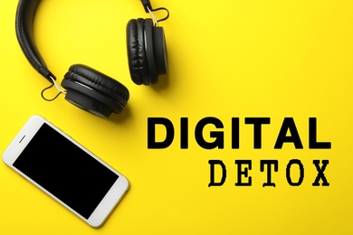 Text Digital Detox, stylish headphones and modern phone on yellow background, flat lay