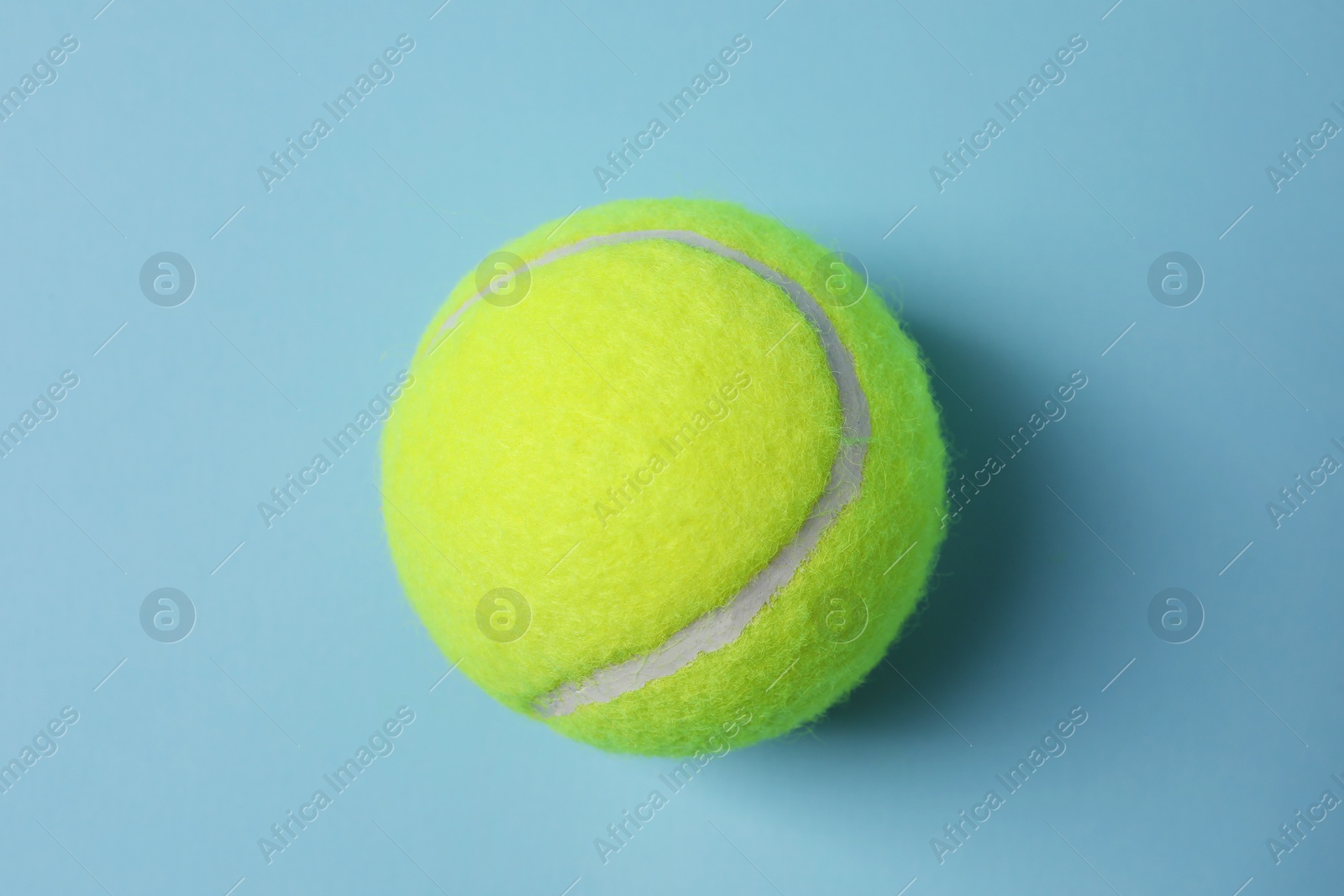 Photo of One tennis ball on light blue background, top view