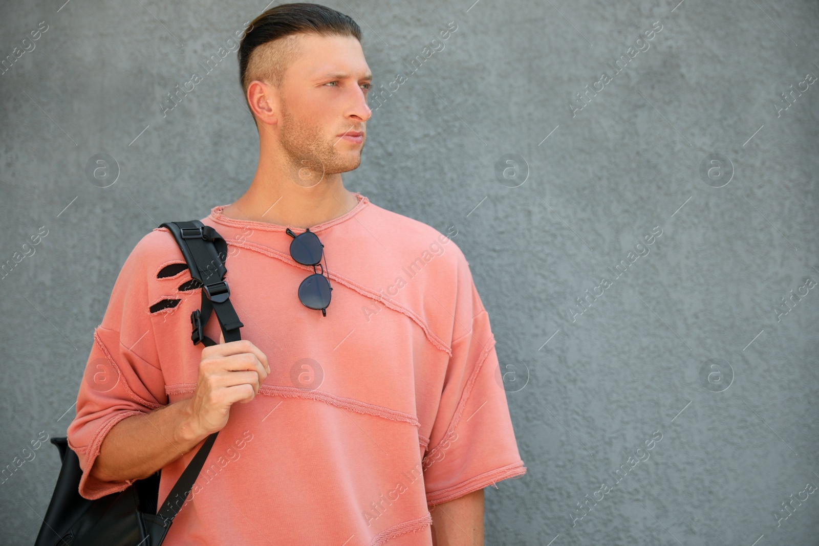 Photo of Handsome young man with stylish sunglasses and backpack near grey wall, space for text