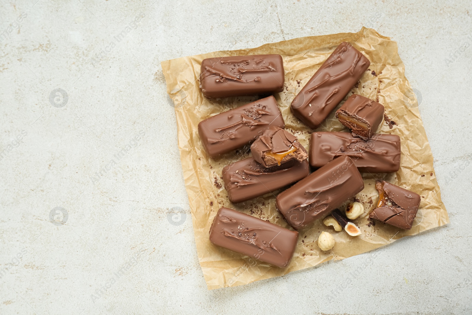 Photo of Delicious chocolate candy bars with caramel and nuts on light table, top view. Space for text