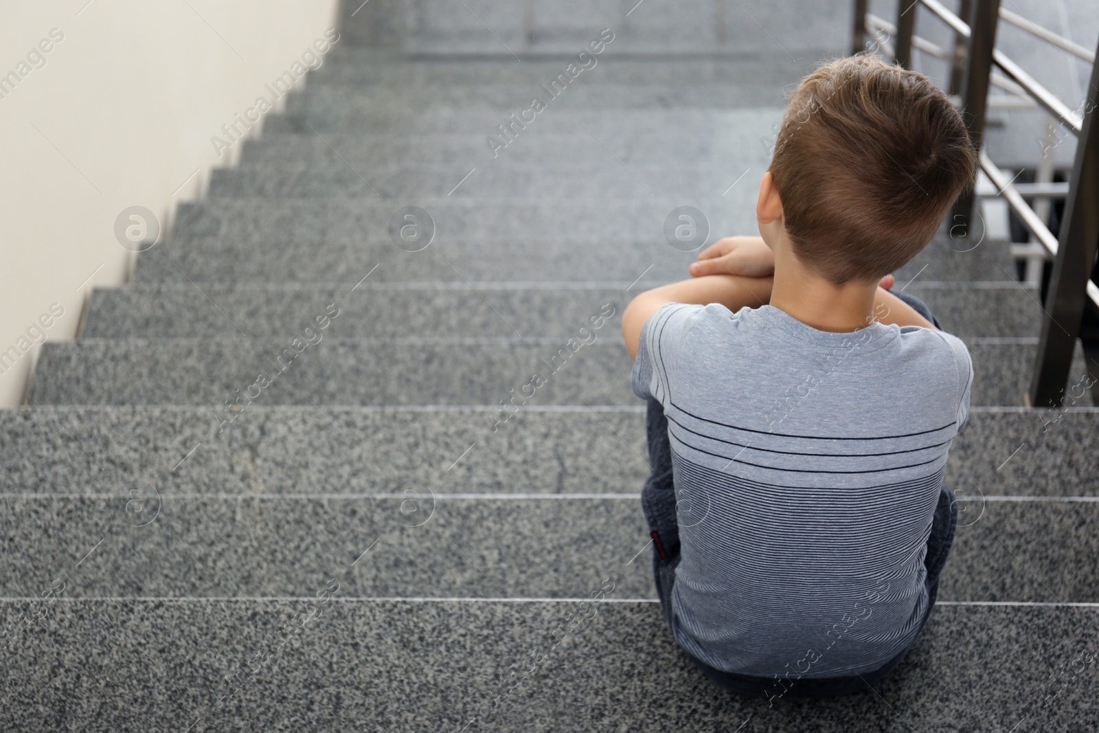 Photo of Lonely little boy sitting on stairs. Autism concept