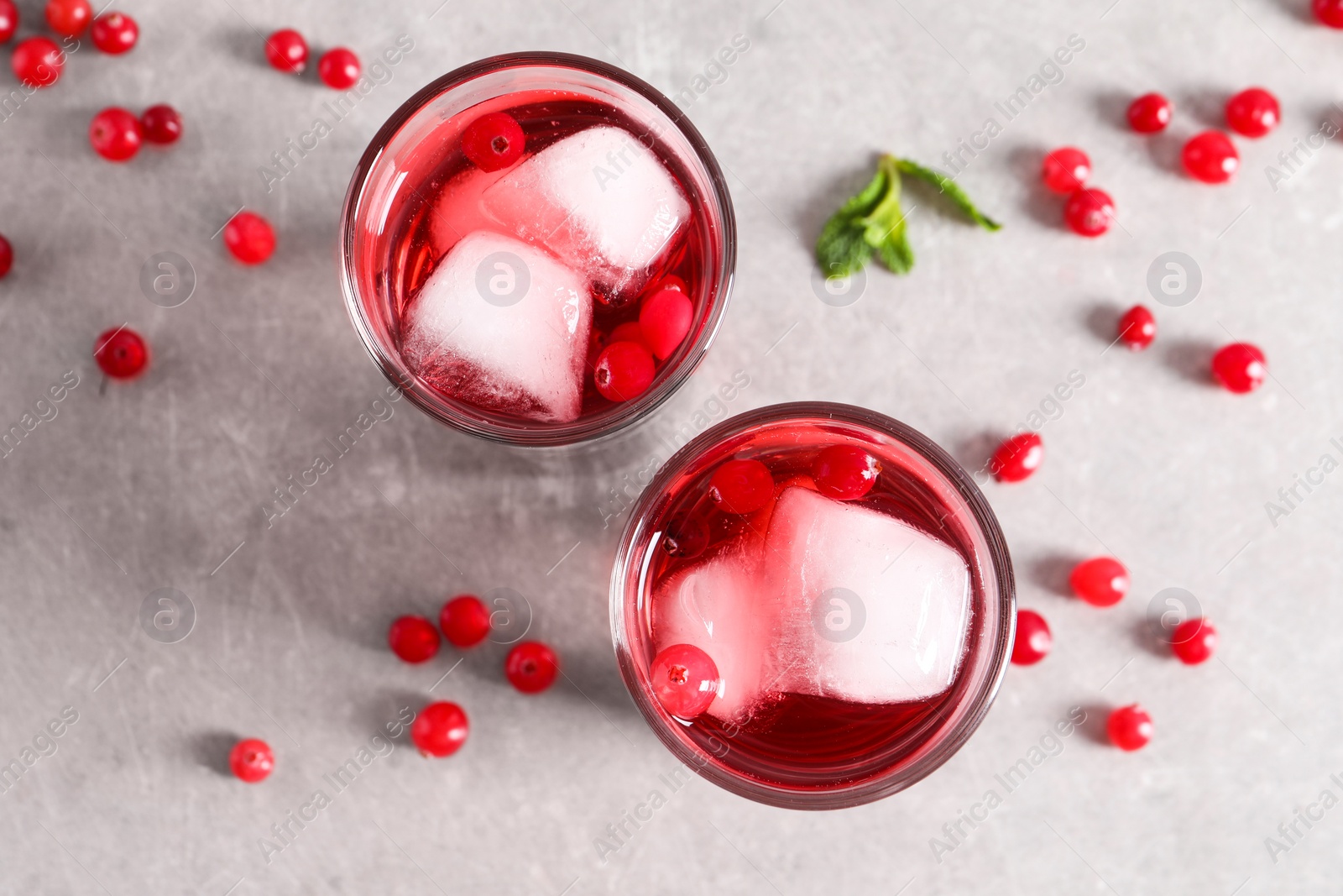 Photo of Tasty cranberry juice with ice cubes in glasses and fresh berries on light grey table, flat lay