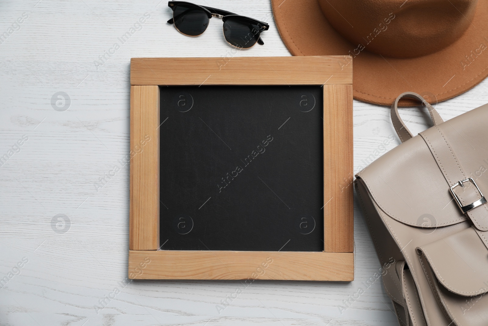 Photo of Blank chalkboard with stylish accessories on white wooden table, flat lay. Space for text