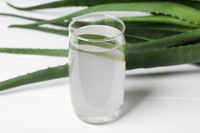 Photo of Fresh aloe juice in glass and leaves on white wooden table, closeup