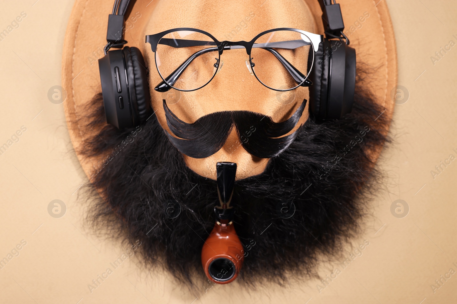 Photo of Man's face made of artificial mustache, beard, glasses and hat on beige background, top view