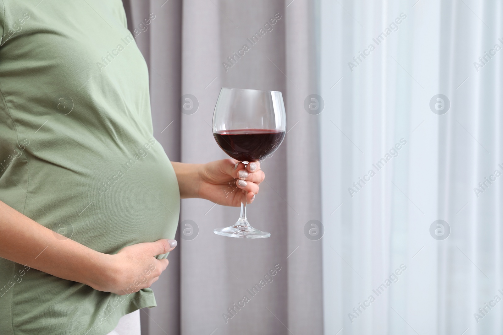 Photo of Future mother with glass of wine indoors, closeup. Alcohol abuse during pregnancy