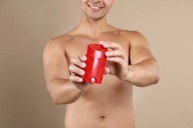 Young man holding deodorant on beige background, closeup. Mockup for design