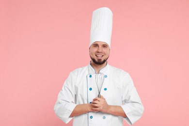 Happy professional confectioner in uniform holding whisk on pink background