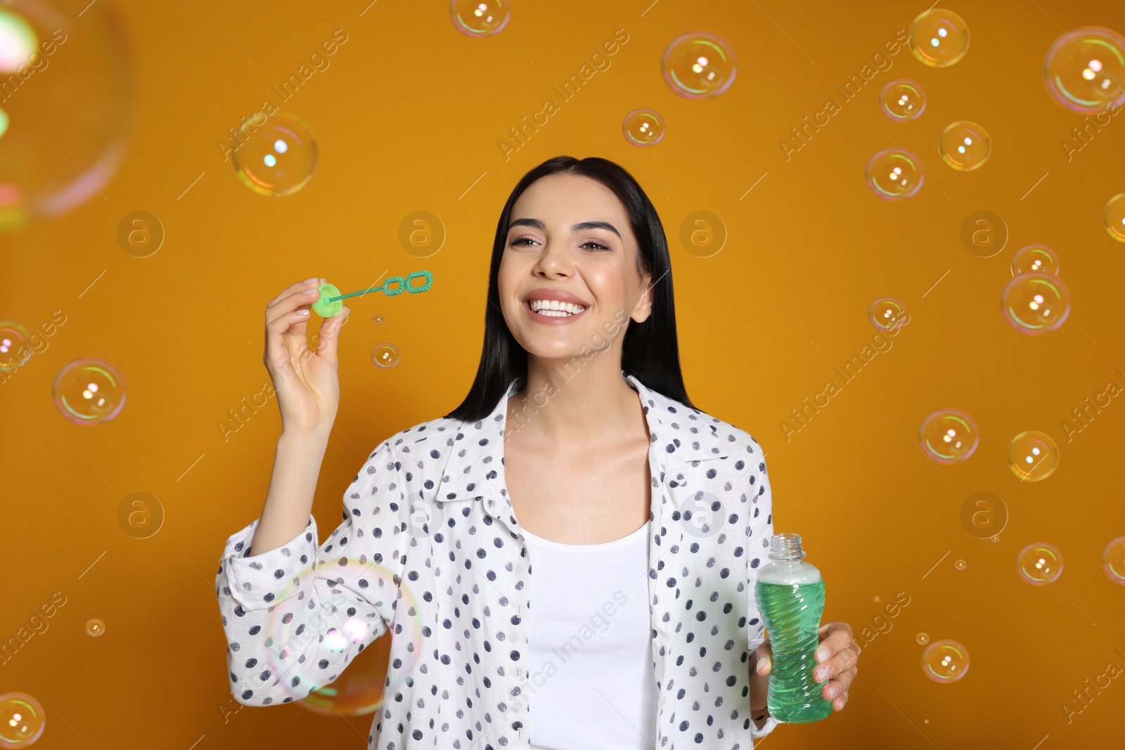 Photo of Young woman blowing soap bubbles on yellow background