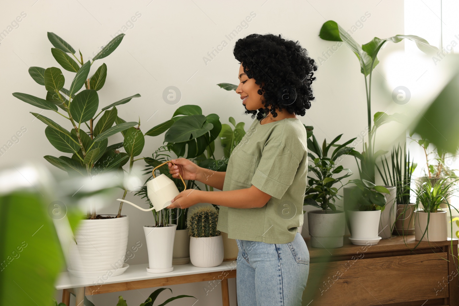 Photo of Happy woman watering beautiful potted houseplants indoors