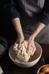 Making bread. Woman kneading dough at wooden table on dark background, closeup