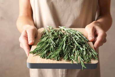 Photo of Woman holding wooden board with fresh rosemary twigs, closeup