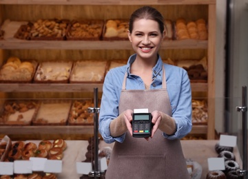 Seller holding payment terminal in bakery. Space for text