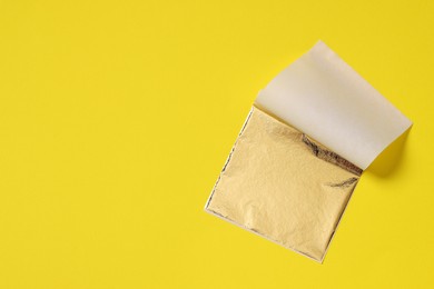 Photo of Edible gold leaf sheet on yellow background, top view. Space for text
