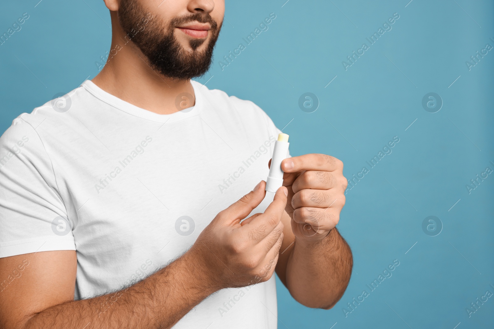 Photo of Young man with lip balm on turquoise background, closeup. Space for text