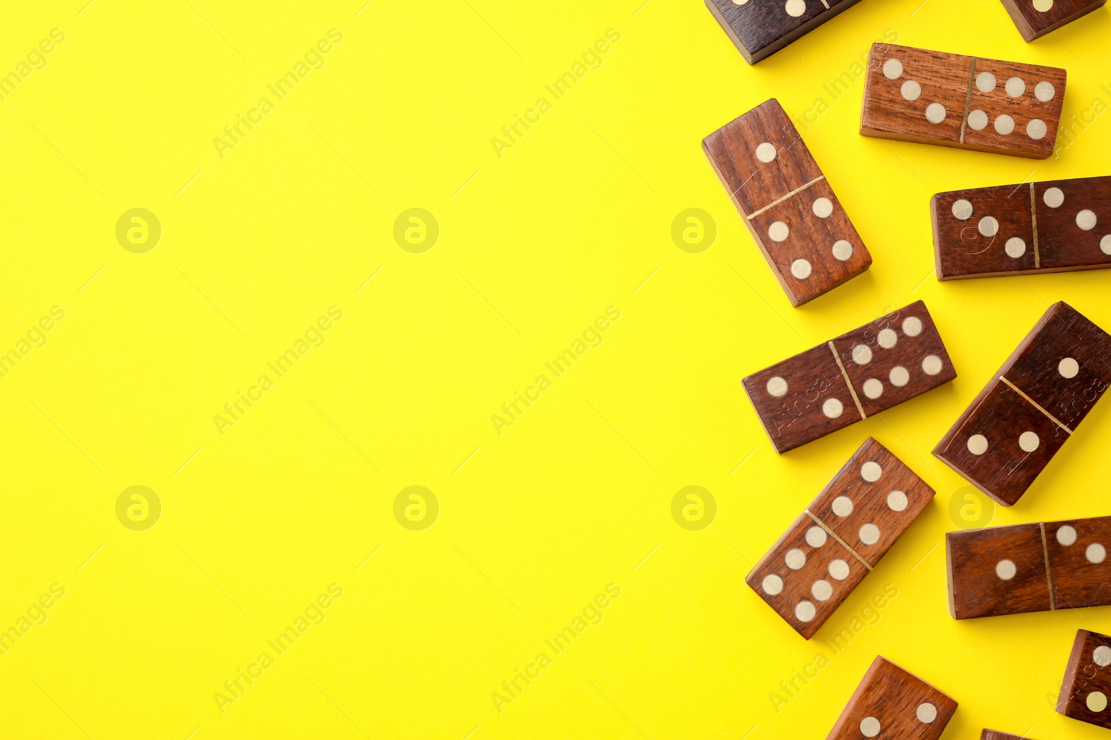 Photo of Wooden domino tiles on yellow background, flat lay. Space for text