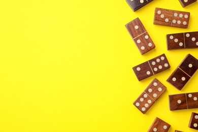 Photo of Wooden domino tiles on yellow background, flat lay. Space for text