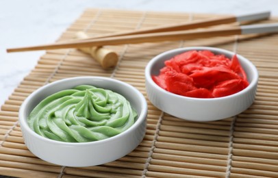 Photo of Bowls with swirl of wasabi paste and pickled ginger on bamboo mat, closeup