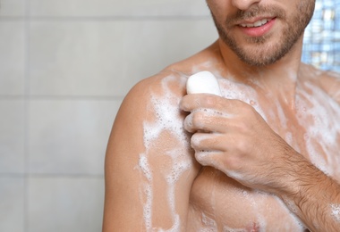 Photo of Young man taking shower with soap in bathroom, closeup. Space for text