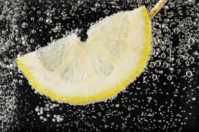 Photo of Juicy lemon slice in soda water against black background, closeup