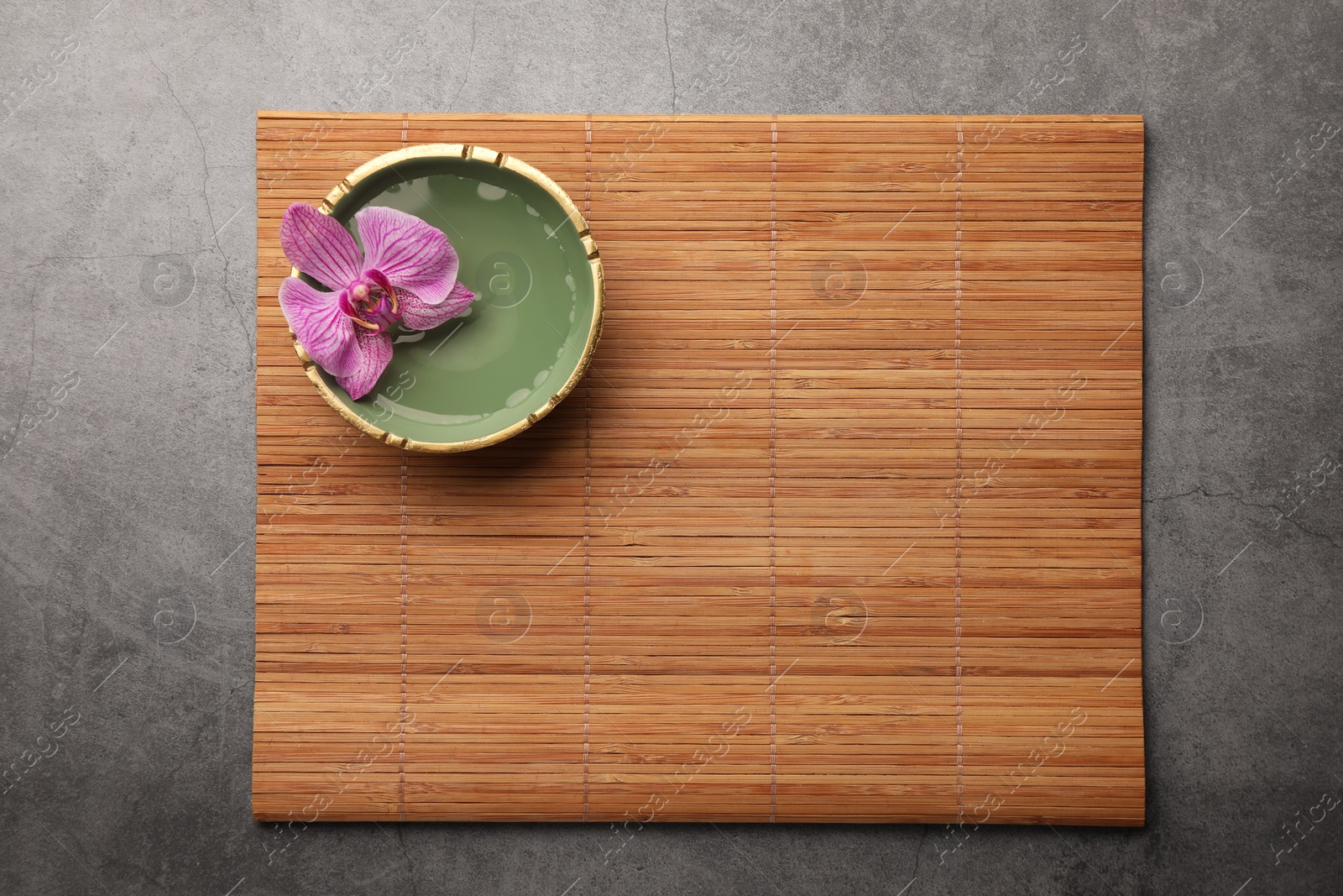 Photo of Bamboo mat and bowl with orchid flower on grey table, top view. Space for text