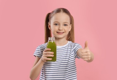 Photo of Cute little girl with glass of fresh juice showing thumbs up on pink background