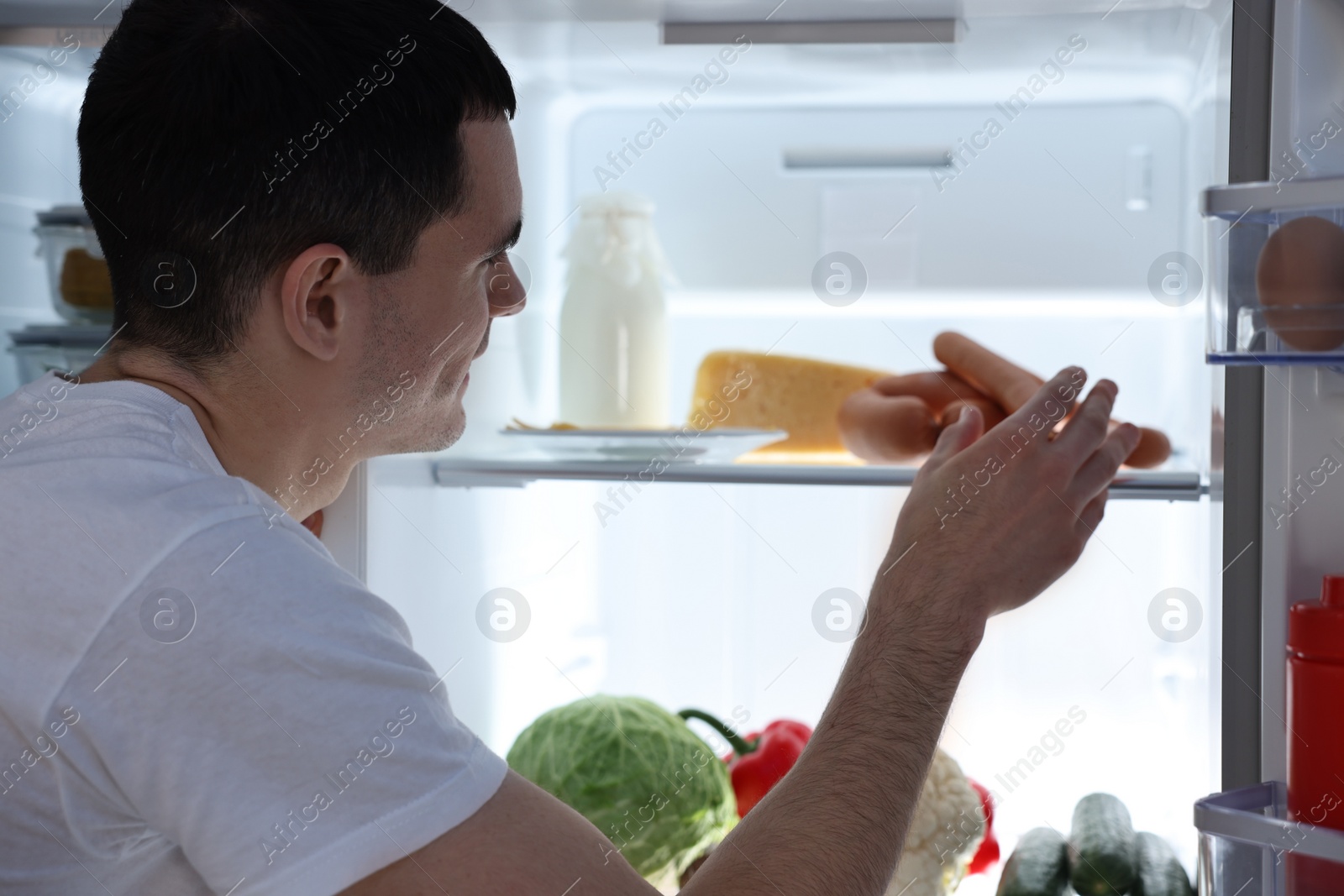 Photo of Man taking sausages out of refrigerator at night