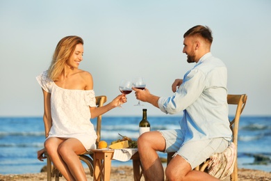 Photo of Young couple with glasses of wine having romantic dinner on beach