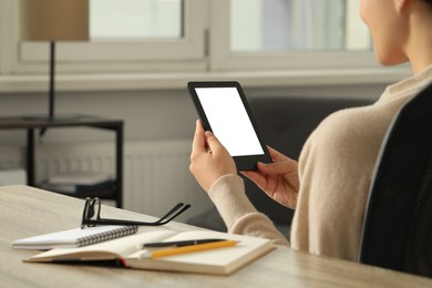 Photo of Young woman using e-book reader at wooden table indoors, closeup. Space for text