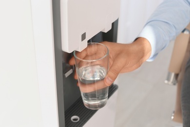 Photo of Man filling glass from water cooler at workplace, closeup