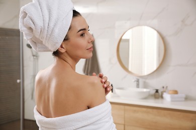 Beautiful young woman with towel on head in bathroom