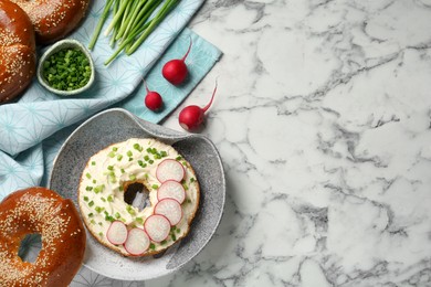 Photo of Delicious bagel with cream cheese, green onion and radish on white marble table, flat lay. Space for text