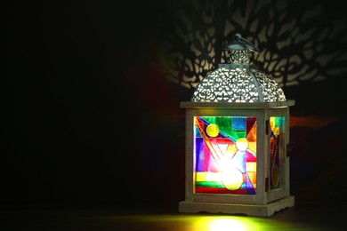 Photo of Decorative Arabic lantern on table against dark background. Space for text